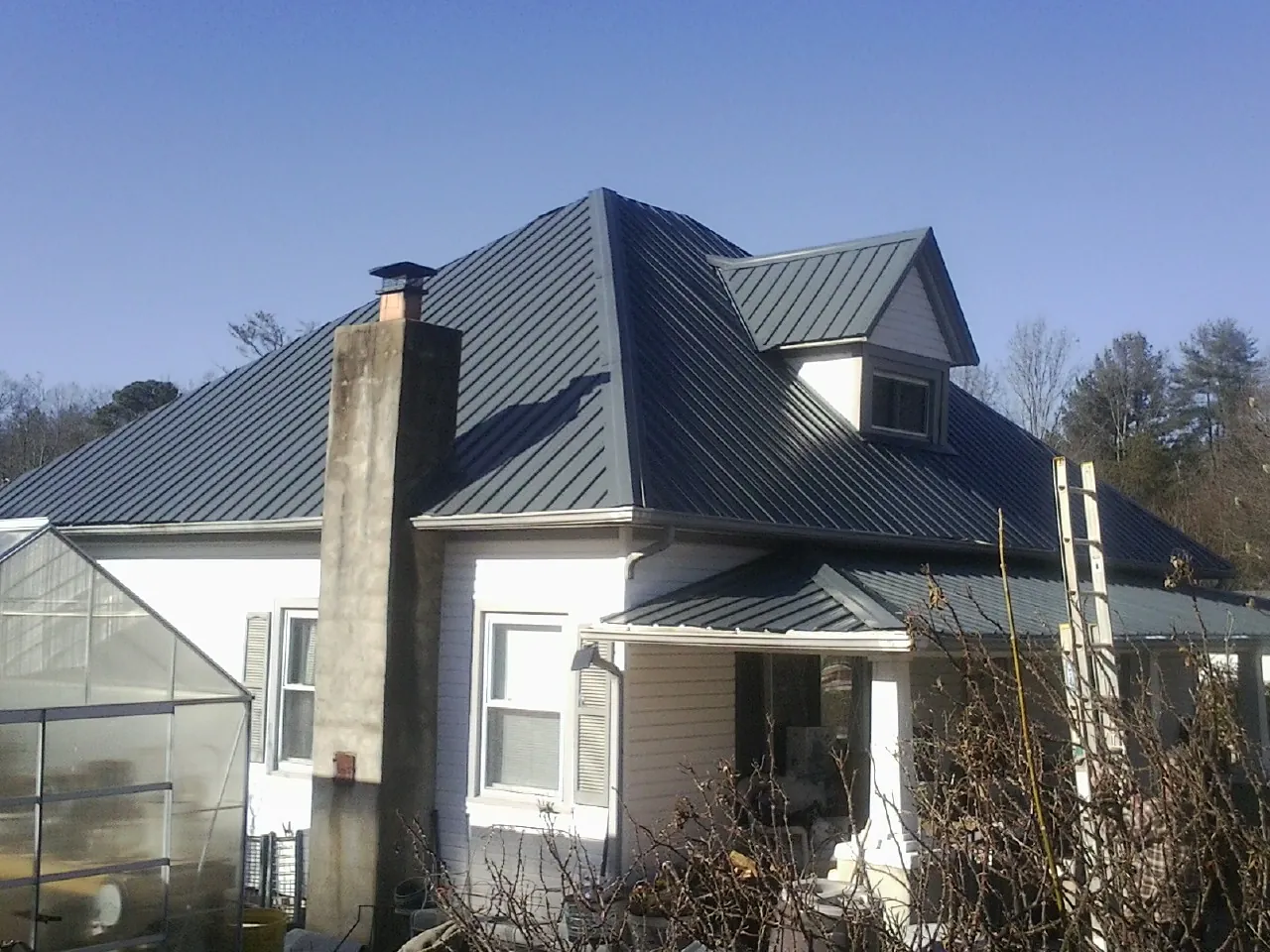 Dark blue standing seam metal roof on a white farmhouse with dormer — Slate & Tile Roof Repair by Roofing Brothers in Sheboygan