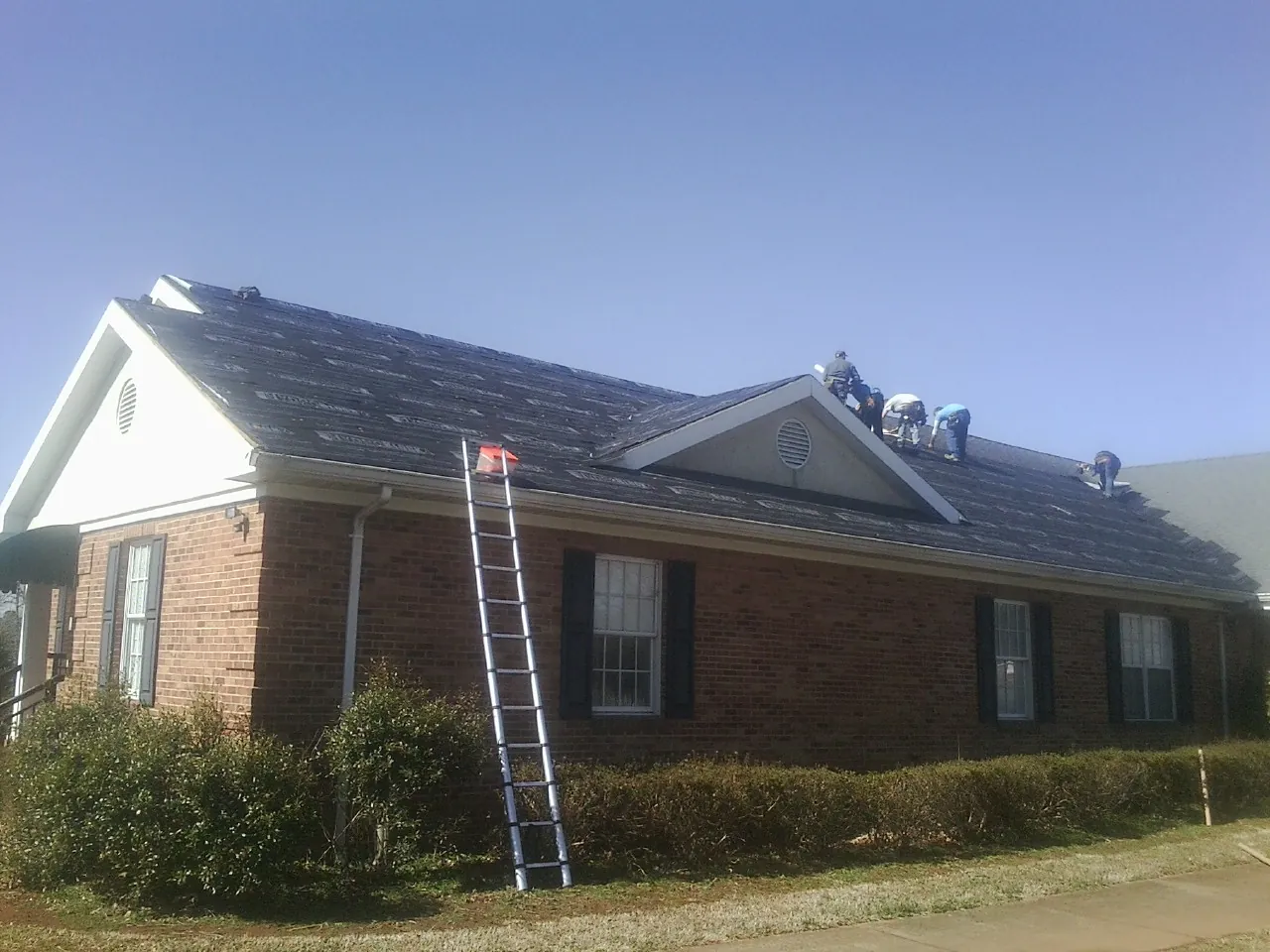 Crew tearing shingles off a brick ranch roof with a ladder set — Emergency Roof Repair work by our crew in Sheboygan