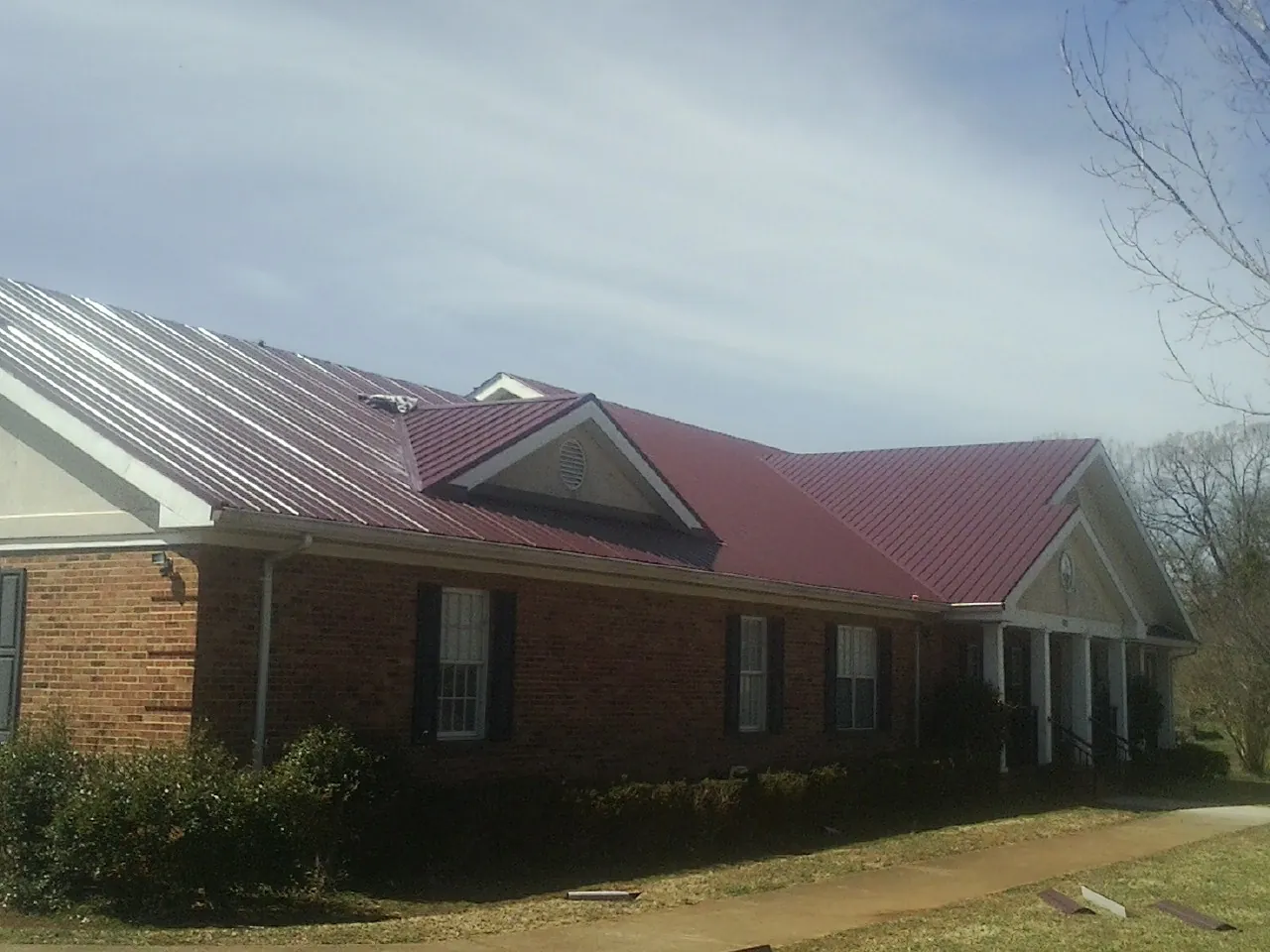 Red metal roof with gabled entries on a long brick building, from a Hail Damage Roof Repair job in Sheboygan