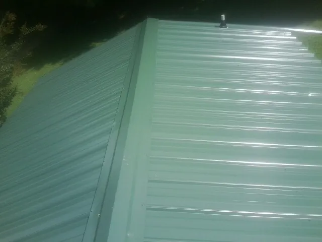 New green metal panels meeting at the ridge of a roof — Flat Roof Repair work by our crew in Sheboygan