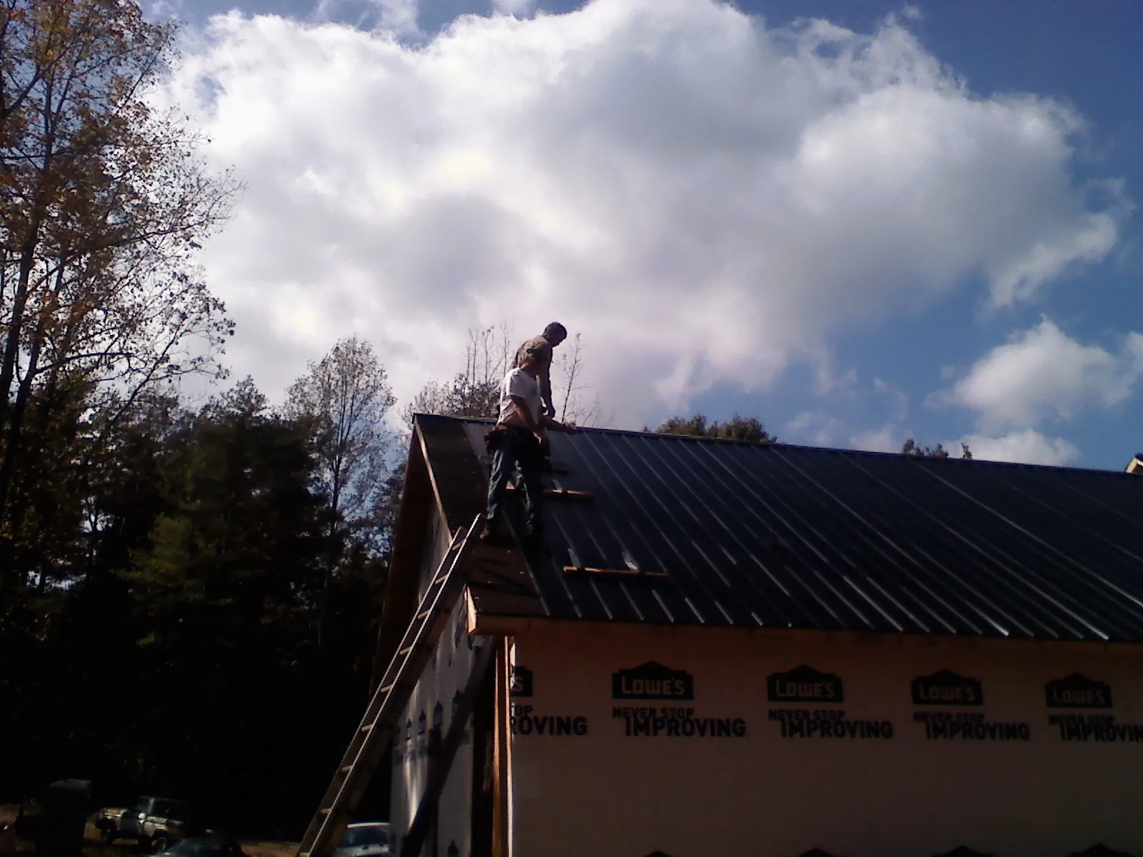 Roofer fastening dark metal panels high against a cloudy sky, from a Roof Inspection job in Sheboygan