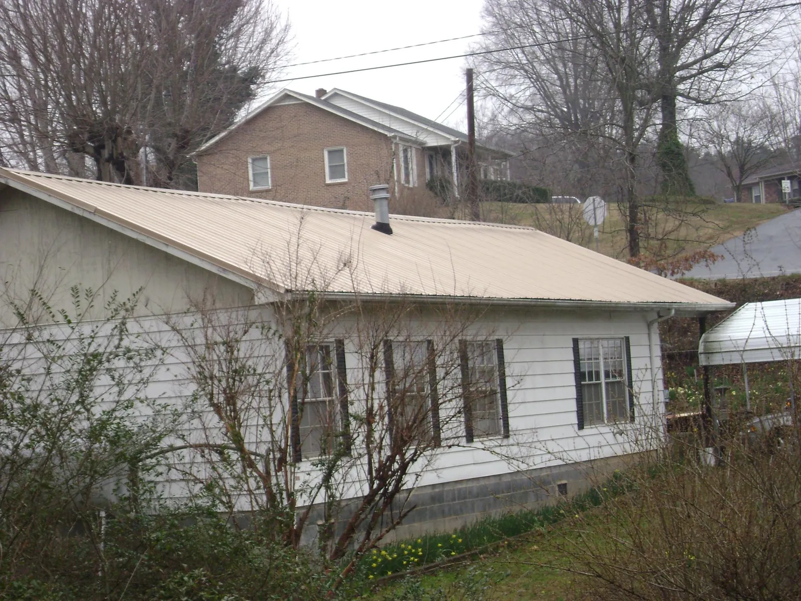Tan metal roof on a white sided house set into a hillside — Commercial Roofing by Roofing Brothers in Sheboygan