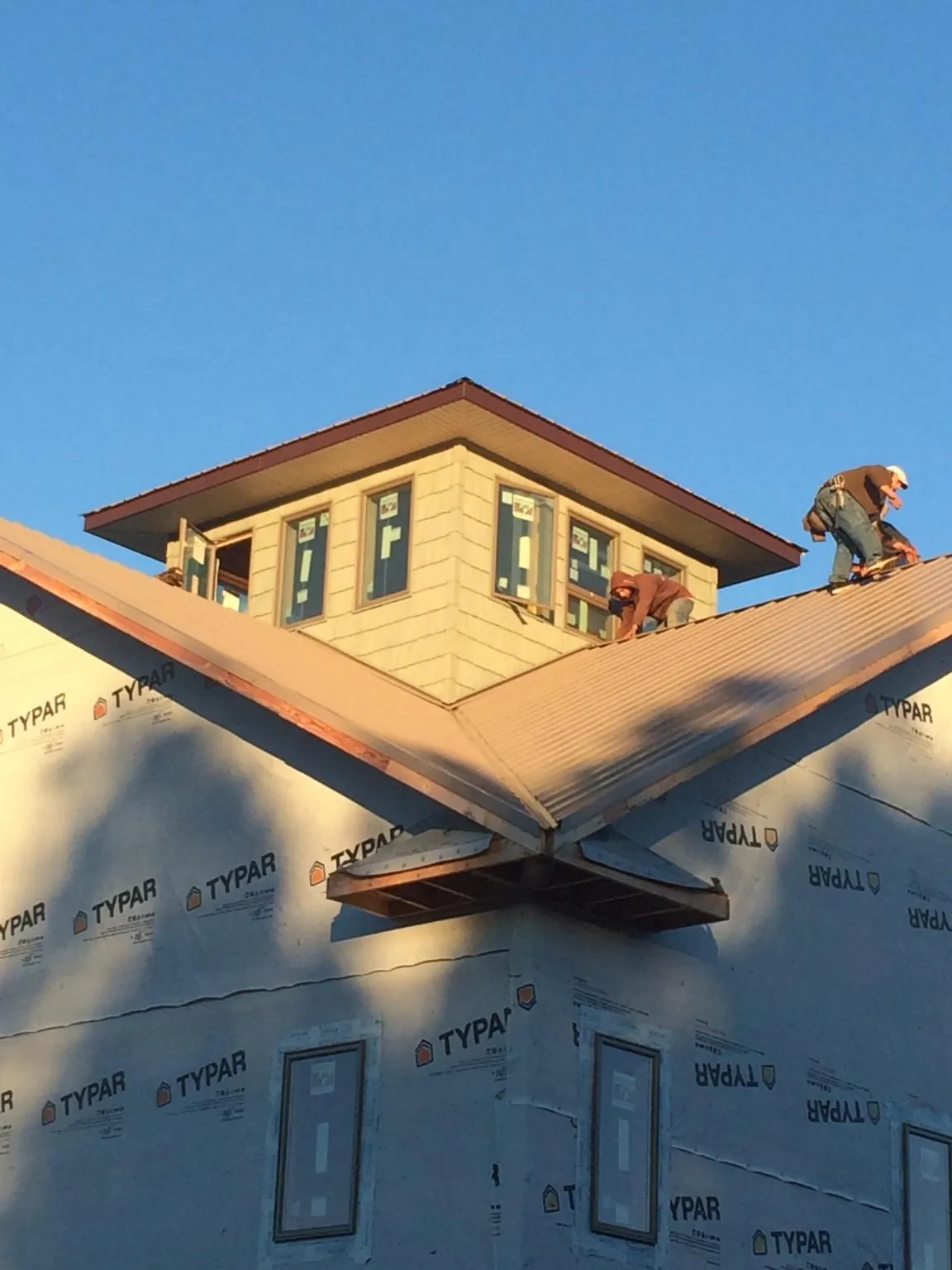 Roofers working around a rooftop cupola on a new metal roof at sunset — Roof Waterproofing in Sheboygan by Roofing Brothers